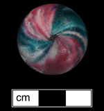 18BC27 - Handmade glass marble in a variety known as solid core swirl. Dates from the 1850s through at least the 1890s (Gartley and Carskadden 1998:127-129). Cut-off marks visible at either “pole” of the marble (at the center of the overall marble photo and the small central scar in the detail shot to the right) - click on image to see larger view of both.